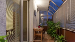 Ein schmales, abgeschlossenes Patio mit Tisch und Stühlen, umgeben von Topfpflanzen und Blick auf den Himmel durch eine Dachfenster.