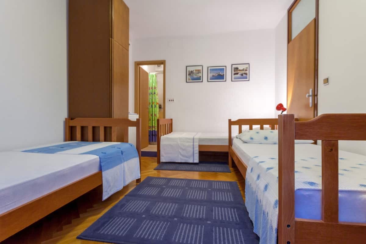 A dormitory room with three wooden bunk beds, a small wooden wardrobe, and a door leading to another room.