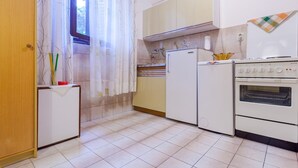 Eine kleine Küche mit Kühlschrank, Herd und einem Fenster mit Vorhängen.