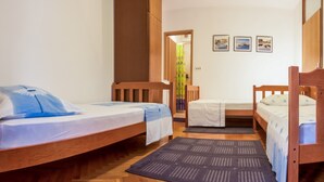 Ein Zimmer mit zwei Holzbetten, einem kleinen Tisch und einem Stuhl. An der Wand hängen drei gerahmte Bilder.