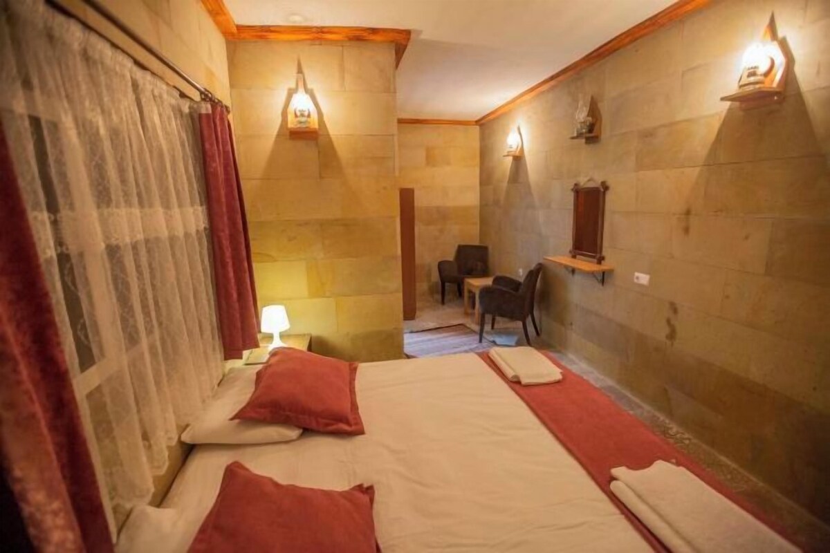 Una stanza con un letto, due cuscini, un comodino, una sedia e un tavolino.
