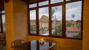 A dining area with a table and chairs, large windows with a view of buildings and hot air balloons. - Capiedra Hotel (Nevsehir)