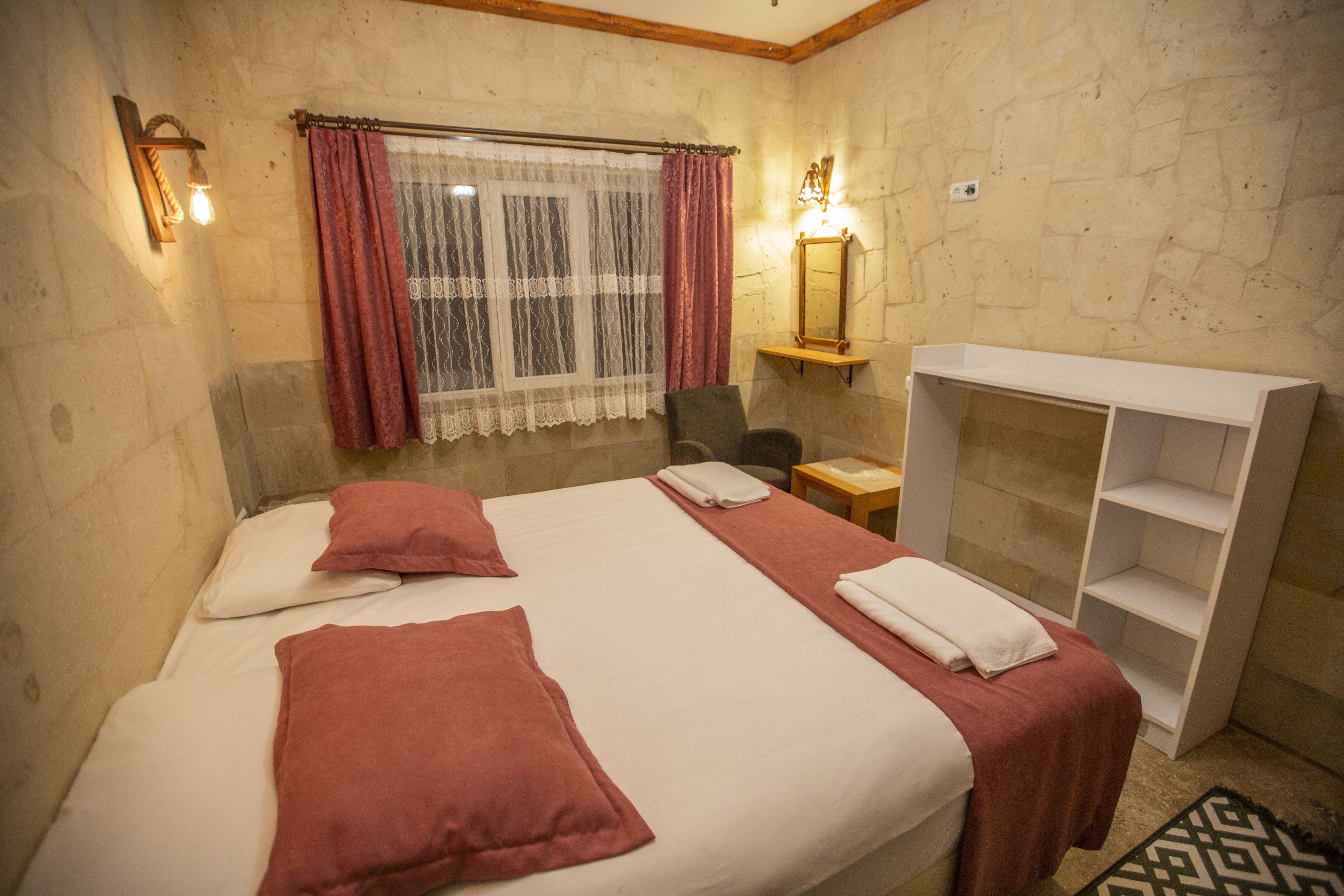 A hotel room with a large bed, two pillows, a nightstand, a mirror, and a shelf unit.