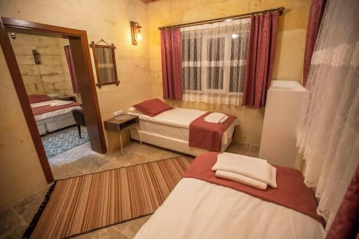 Ein Zimmer mit zwei Betten, einem Spiegel, einem Fenster mit Vorhängen und einem kleinen Tisch.