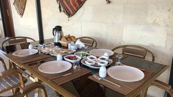 Una mesa de comedor dispuesta con platos, tazones y diferentes alimentos, rodeada de sillas.