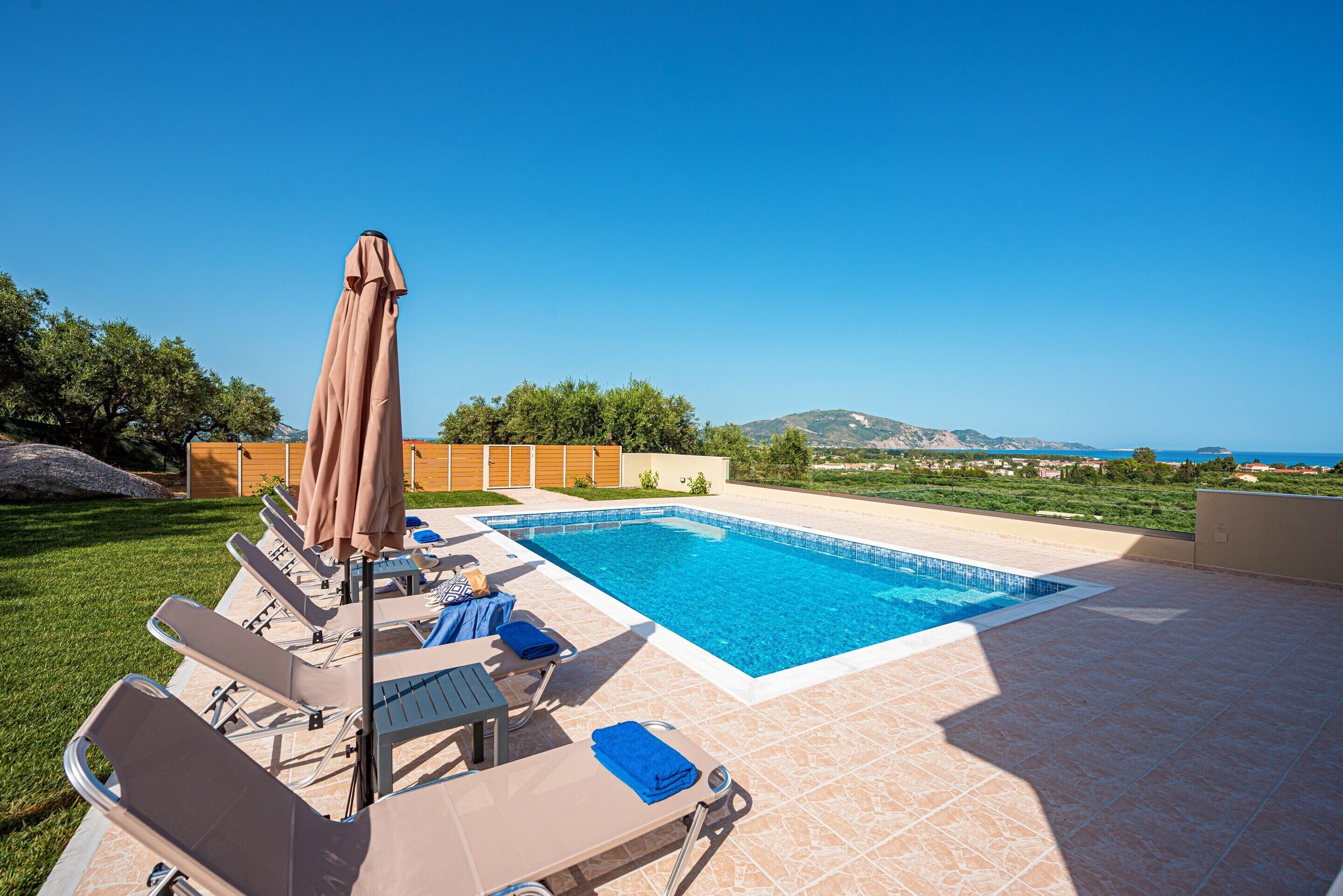 Ein Poolbereich mit Liegestühlen und Sonnenschirm, strahlend blauer Himmel und Blick auf die Landschaft.