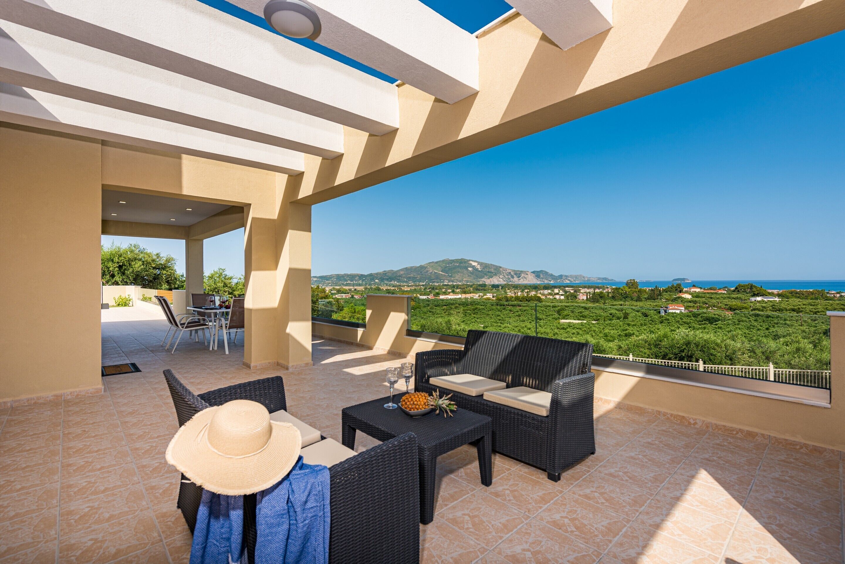 Un patio al aire libre con mobiliario de mimbre, una mesa de comedor y vistas al mar y a las montañas.