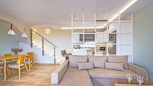 Un salon moderne avec un canapé d’angle, une table à manger en bois et des luminaires suspendus.