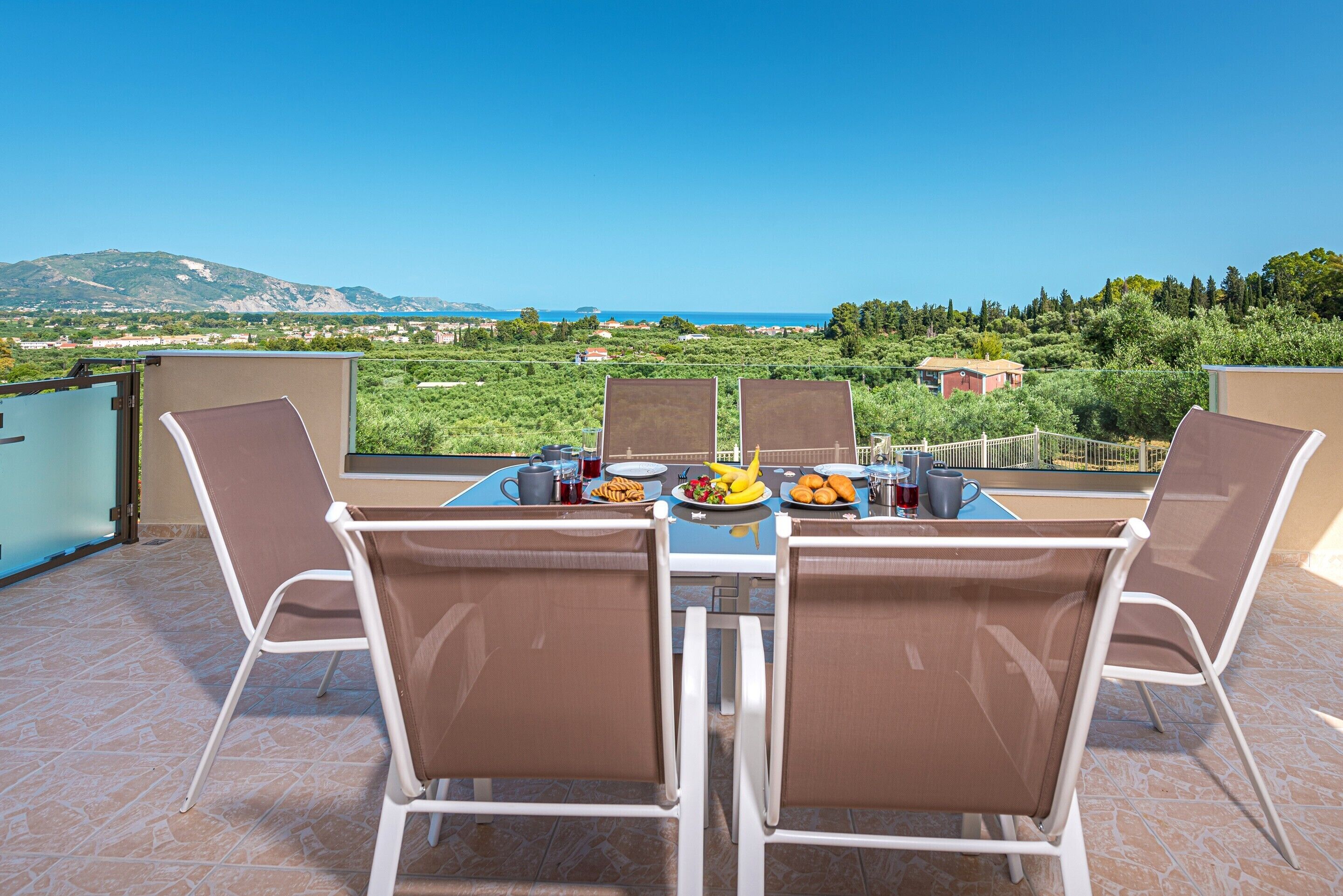 Una terraza con una mesa para dos, con vista a un paisaje pintoresco que incluye montañas y una masa de agua.