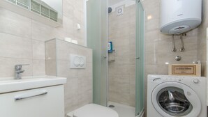 Une salle de bain moderne équipée de toilettes, d’un lavabo, d’une douche à parois de verre et d’un lave-linge à chargement frontal.