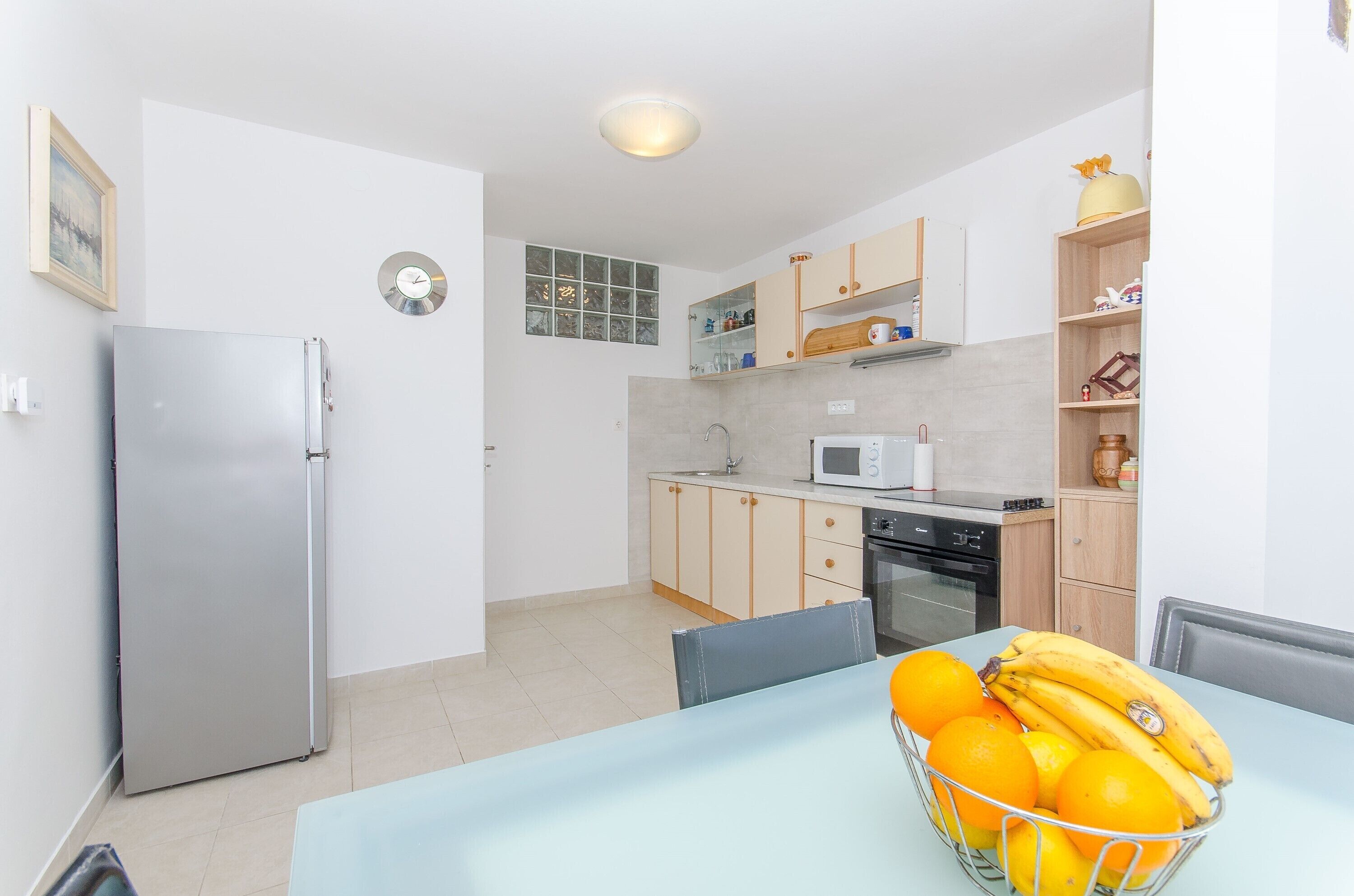 Una cocina moderna con refrigerador, microondas y horno. Hay una mesa de comedor con una cesta de frutas.