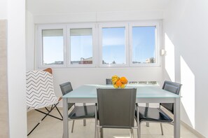 A dining area with a glass table, four chairs, a bowl of fruit, and a window with blinds. - Spacious apartment Neven near center, with two AC units (Split)