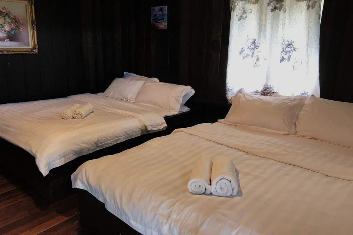 Two beds with white linens and rolled towels, a painting on the wall, and a window with floral curtains.