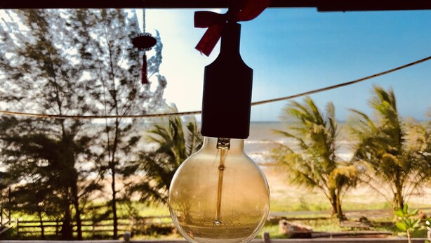 A hanging light bulb with a red bow, wooden benches, and a view of palm trees and a beach. - Tim's Seaside Hideout Resort (Miri)