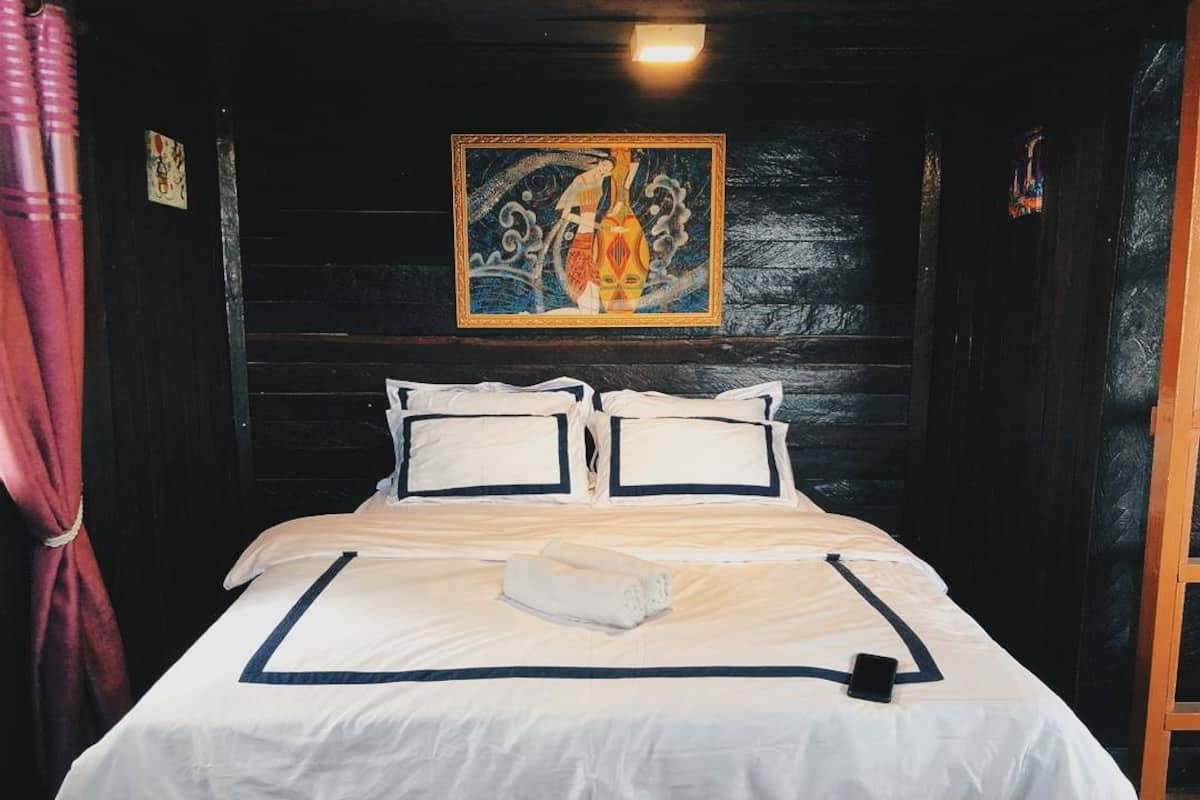 A neatly made bed with a white and navy blue bedspread, a rolled towel, and a smartphone on the bed.