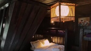 A cozy, rustic bedroom with a wooden headboard, a small bedside table with a white cloth, and a hanging light fixture. - Tim's Seaside Hideout Resort (Miri)