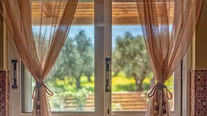 Una ventana con cortinas translúcidas recogidas, mostrando una vista de vegetación al exterior.