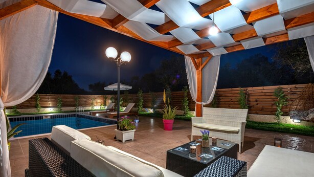 Un patio exterior con piscina, mobiliario de mimbre y plantas en macetas.