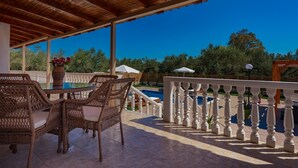 Un patio cubierto con mobiliario de mimbre, una piscina y una barandilla blanca.