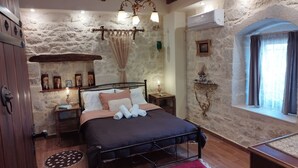 A bedroom with a stone wall, a bed with a black frame, a wooden ceiling, and a window with curtains. - Cozy traditional stone-house at Cretan nature .Stunning... (Βασιλικη)