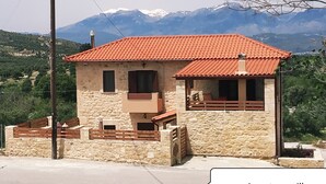 A stone building with a red-tiled roof, a balcony, and a view of mountains in the background. - Cozy traditional stone-house at Cretan nature .Stunning... (Βασιλικη)