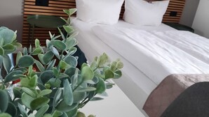 A hotel room with a wooden headboard, a bed with white linens, a small table with a plant, and a green chair. - Hotel Freihof am Roland (Wedel)