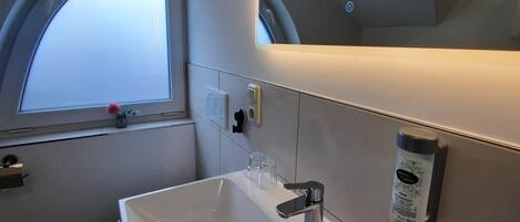 Un baño moderno con un lavamanos blanco, un espejo con luz circular y una ventana con vistas al cielo.
