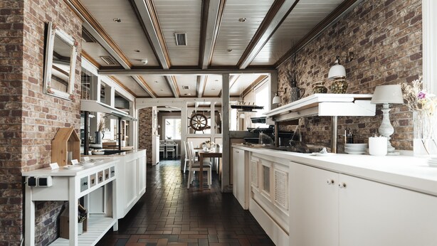 A modern kitchen with exposed brick walls, white cabinetry, and a herringbone patterned floor. - Hotel Freihof am Roland (Wedel)