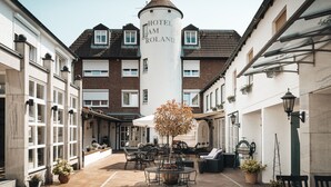 A hotel courtyard with a central tower labeled "Hotel Am Roland," surrounded by buildings with large windows and outdoor seating areas. - Hotel Freihof am Roland (Wedel)