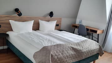 A modern hotel room with a large bed, wooden headboard, and a desk with a chair.