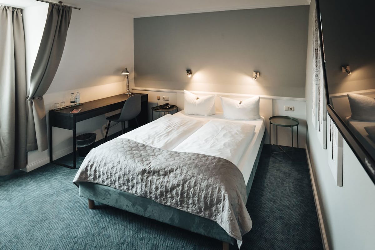 A hotel room with a bed, desk, chair, and bedside lamps.