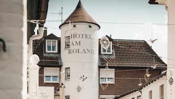 A white cylindrical tower with the text "HOTEL AM ROLAND" on its side, surrounded by traditional European buildings with tiled roofs and visible windows.