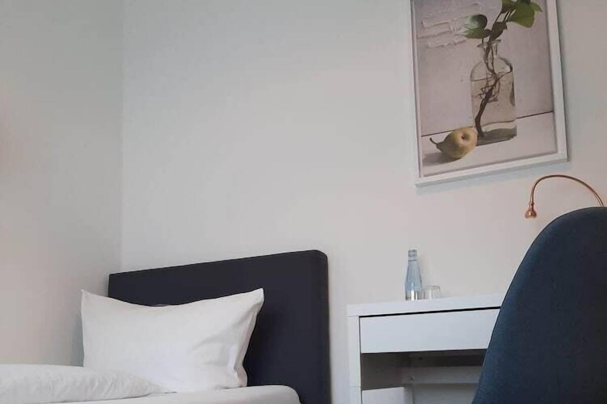 A bedroom with a bed, a desk, a chair, and a wall-mounted picture.
