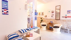 A modern living room with a sofa set, a coffee table, and two white chairs. There are artworks on the walls and a stone wall in the background. - Apartments Dalmacija (Omis)