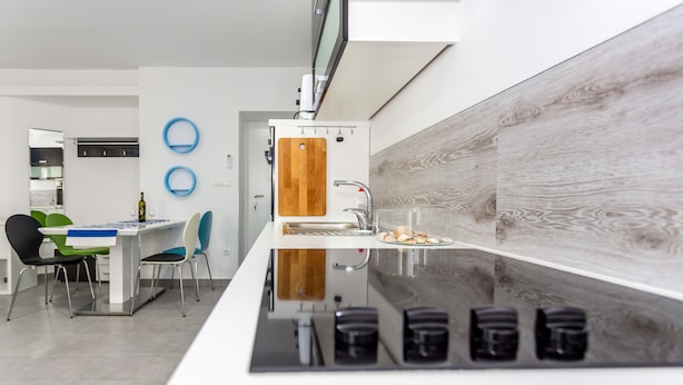 A modern kitchen with a central island, a dining area with chairs, and a wooden cutting board on the wall. - Apartments Dalmacija (Omis)