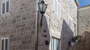 A stone building with a staircase leading to a door, a street lamp, and a small plant on the steps. - Apartments Dalmacija (Omis)