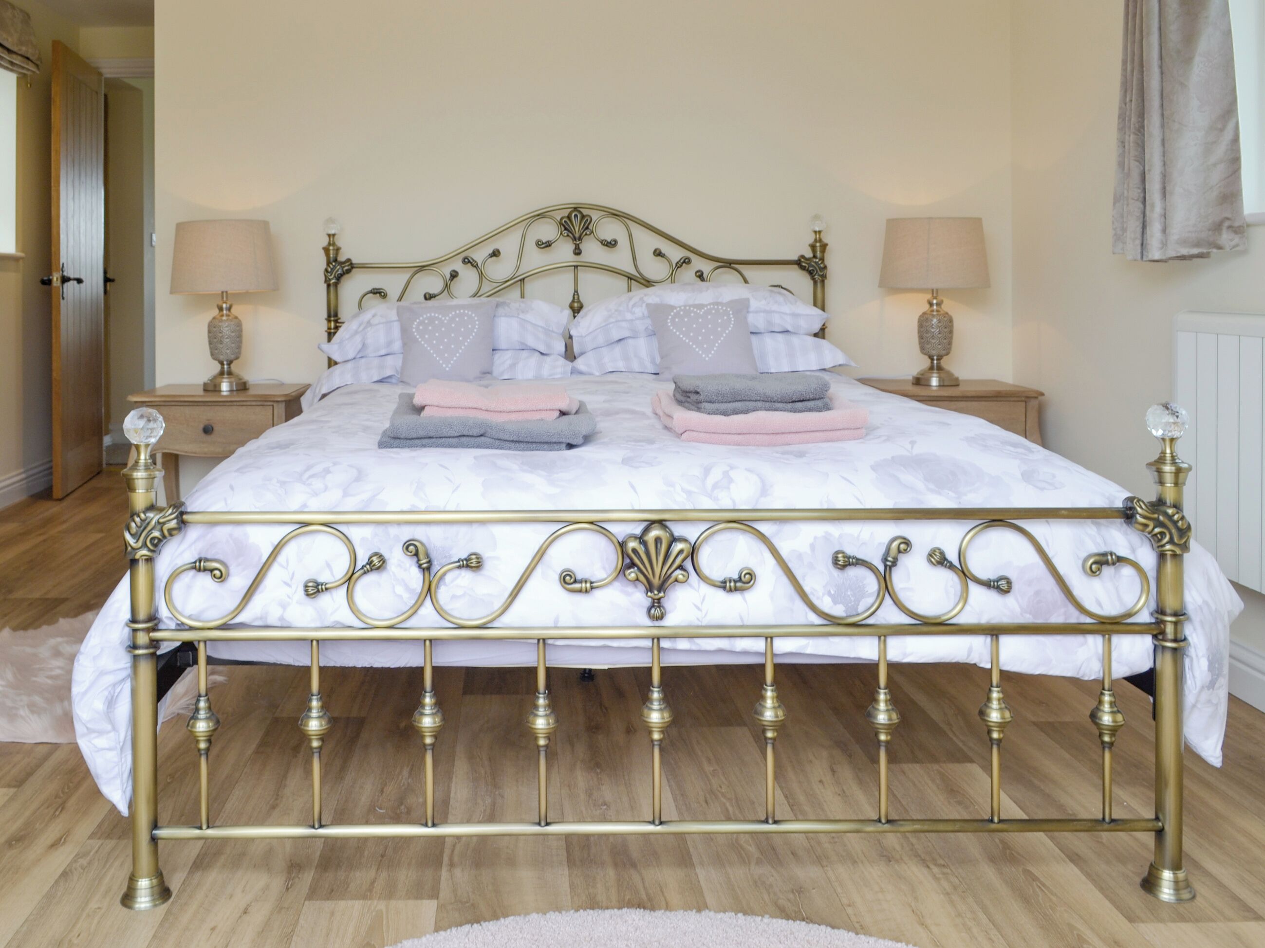 Un lit avec une tête de lit et un pied de lit en métal décoratif, deux tables de chevet avec des lampes et un plancher en bois.
