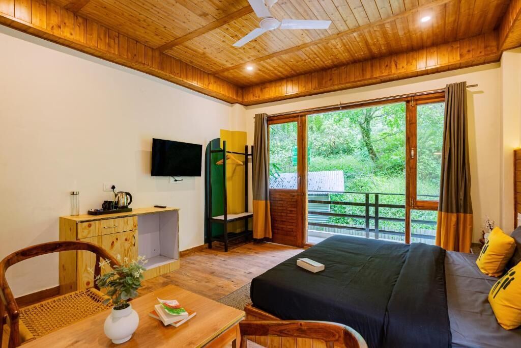 A wooden-floored room with a bed, a TV, a desk, and a window with a view of greenery.