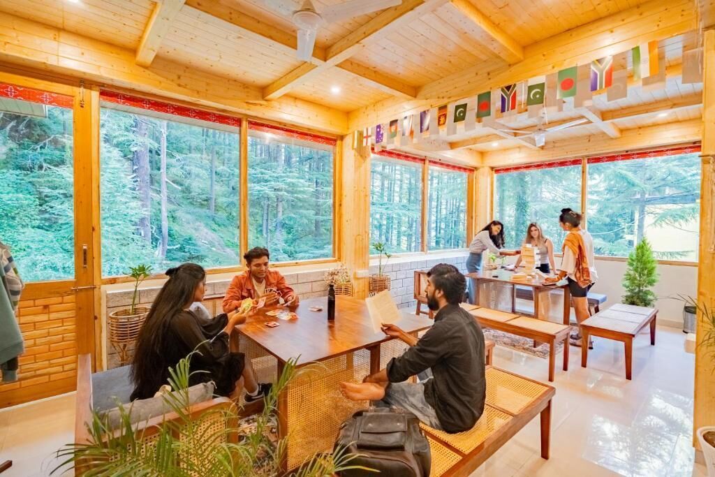 Interior de madera con amplios ventanales, un grupo de personas sentadas en una mesa y un pequeño árbol de Navidad.