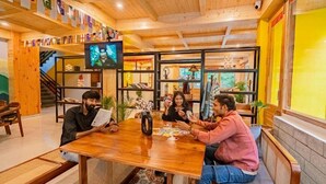 A wooden interior with a group of people playing cards at a table. - The Hosteller Kasol (Bhuntar)
