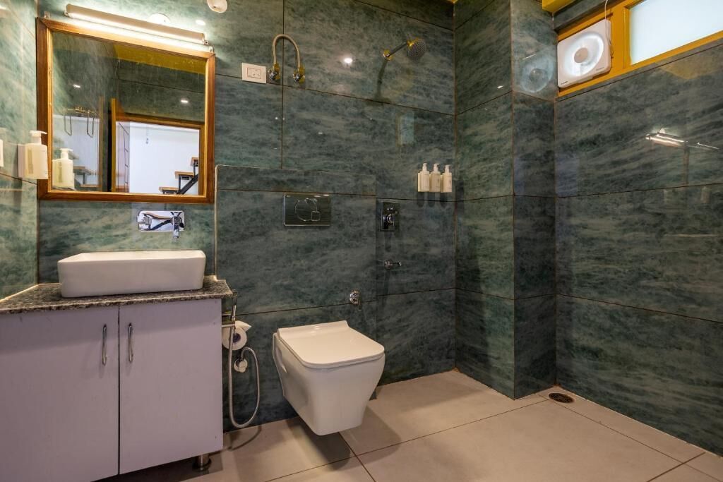 A modern bathroom with a marble wall, a white sink, a toilet, and a shower area.