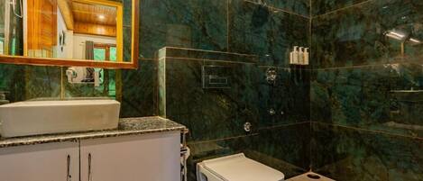 A bathroom with a marble wall, a sink, a toilet, and a shower area.