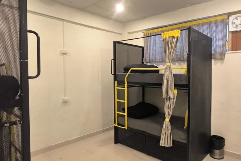 A bunk bed with a ladder, a small window with curtains, and a wall-mounted fan.