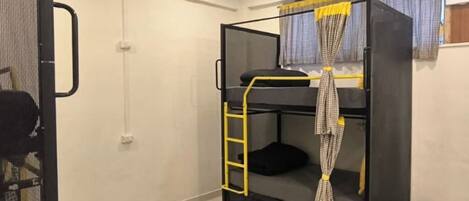 A bunk bed with a ladder, a small window with curtains, and a wall-mounted fan.