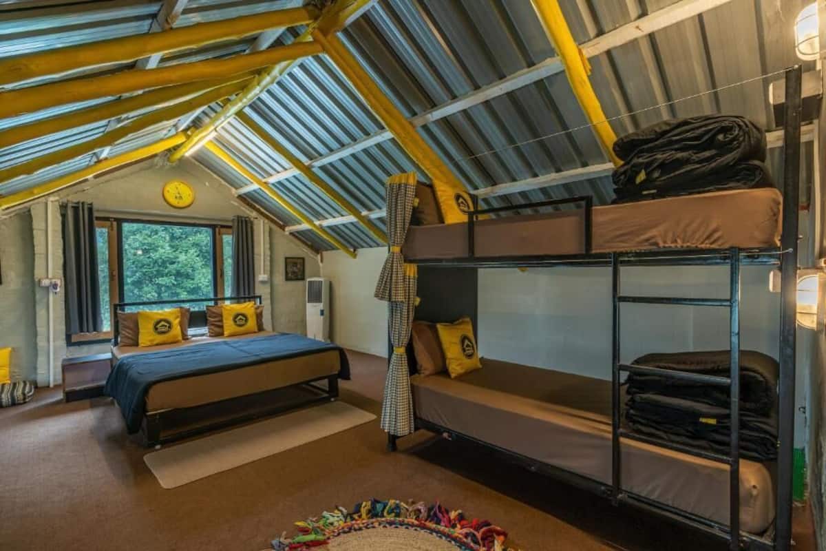 A compact room with a bunk bed, a single bed, a window with curtains, a clock, and a small rug.