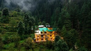 A multi-story building with a green roof, surrounded by dense forest and mist. - The Hosteller Kasol (Bhuntar)