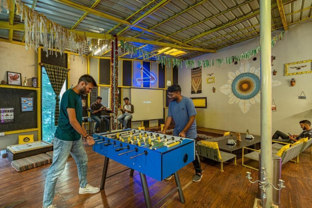 Una habitación con una mesa de fútbol de mesa, suelo de madera y un grupo de personas realizando distintas actividades.