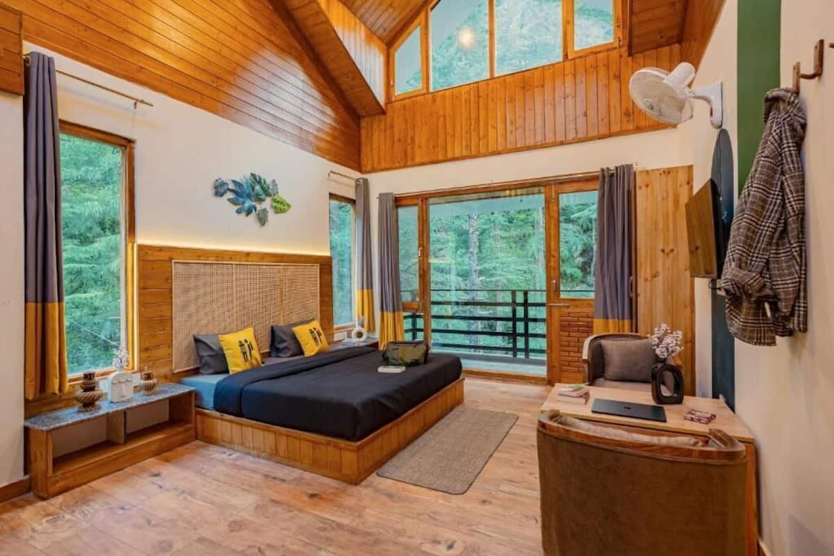 A bedroom with a large bed, wooden walls, and a view of the forest.