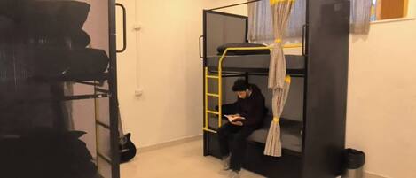 A bunk bed with a ladder, a small trash bin, and a window with curtains.