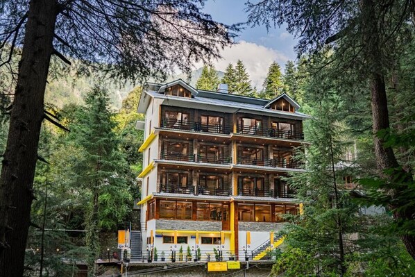 Un chalet à plusieurs étages doté de balcons, entouré d’une forêt dense.